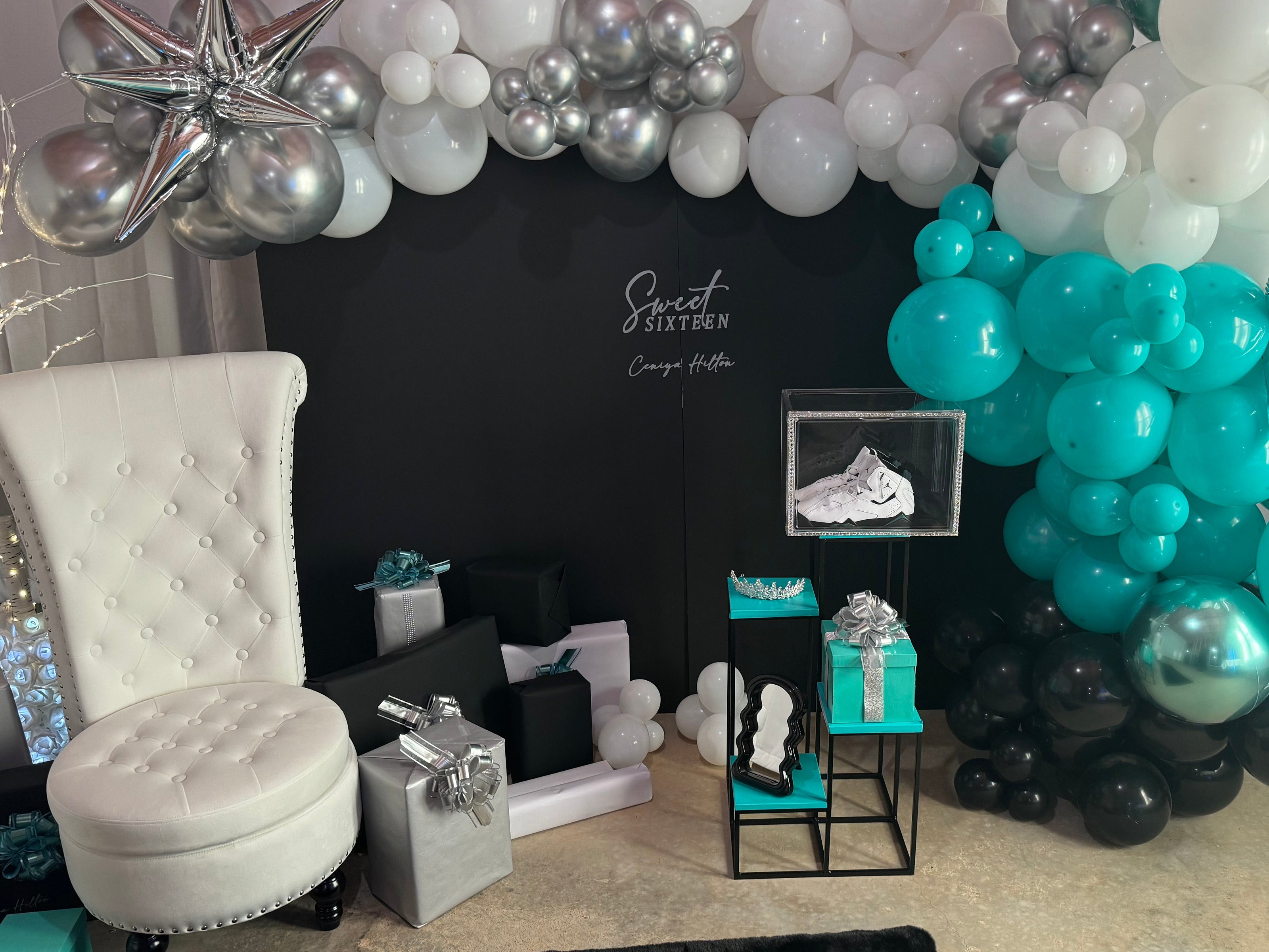 Decorative balloon arch with teal, silver, and black balloons in a room setting.